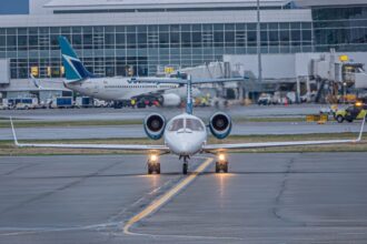 A private jet on the runway at a bustling airport with commercial planes and terminal in view.